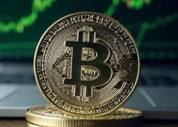 Imagen de bitcoin sobre un escritorio con gráficas verdes en el fondo.
