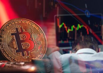 moneda de bitcoin en rojo junto a trader arrepentido frente a computadora con grafico bajista de precio en pantalla y velas de precio superpuestas.