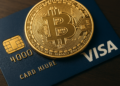 Una moneda de Bitcoin junto a una tarjeta Visa.