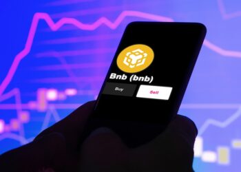 Teléfono en el que se ve el logo de BNB. En el fondo hay un gráfico de precio.