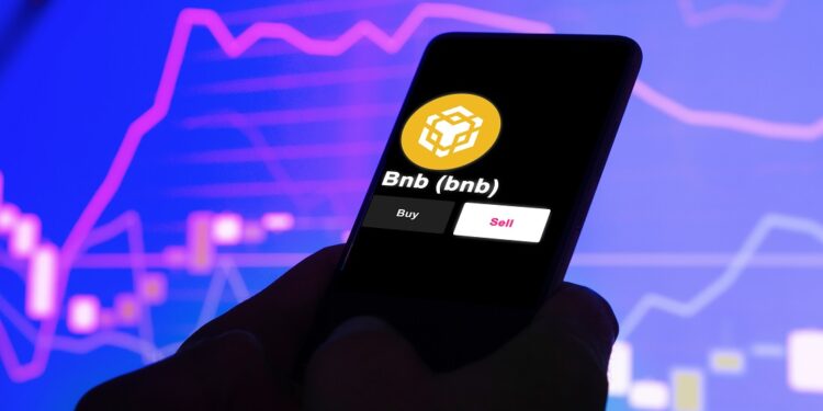 Teléfono en el que se ve el logo de BNB. En el fondo hay un gráfico de precio.