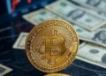 Una moneda de bitcoin sobre varios billetes de dólar.
