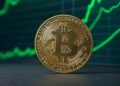 Bitcoin en un escritorio con gráficas en verde en el fondo.