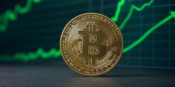 Bitcoin en un escritorio con gráficas en verde en el fondo.