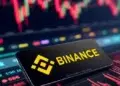 Gráfico de precios junto a un celular con el logo de Binance en su pantalla.