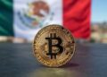 Una moneda dorada de bitcoin delante de la bandera México.