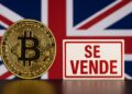 Bitcoin al lado de un letrero de venta y la bandera de Reino Unido de fondo.
