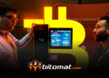 dos hombres conversando junto a minero de bitcoin encendido con logo de bitomat superpuesto