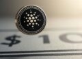 Una moneda de cardano sobre un dibujo de 10 dólares.