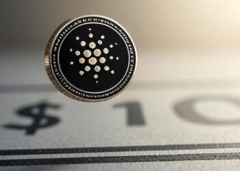 Una moneda de cardano sobre un dibujo de 10 dólares.