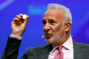 Peter Schiff aparace dando una conferencia y sostiene con su mano derecha una moneda física.