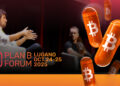 Dos hombres sentados en un sillón, presentes en la conferencia Plan B Lugano 2025 (octubre 24-25). Y para destacar unas cápsulas de color naranja con el logo de Bitcoin