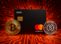 una tarjeta de debito junto a monedas de BTC y USDC.