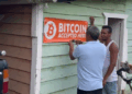 Dos personas colocan un aviso de "se acepta bitcoin" a las afueras de un comercio en República Dominicana.