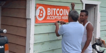 Dos personas colocan un aviso de "se acepta bitcoin" a las afueras de un comercio en República Dominicana.