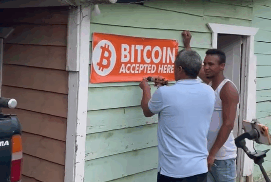 Dos personas colocan un aviso de "se acepta bitcoin" a las afueras de un comercio en República Dominicana.