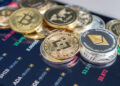 monedas de ethereum, ethereum classic, bitcoin. dogecoin, ripple, cardano y otras apiladas de forma dispersa sobre pantalla de telefono movil con información del rendimiento de prcio del mercado de criptomonedas en pantalla
