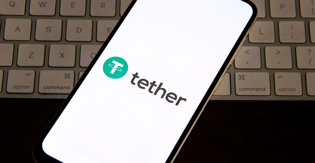 Logo de Tether en un teléfono, arriba de un teclado de computadora.