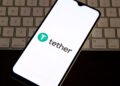 Logo de Tether en un teléfono, arriba de un teclado de computadora.