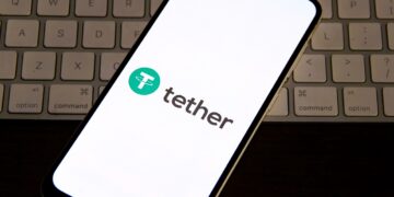 Logo de Tether en un teléfono, arriba de un teclado de computadora.