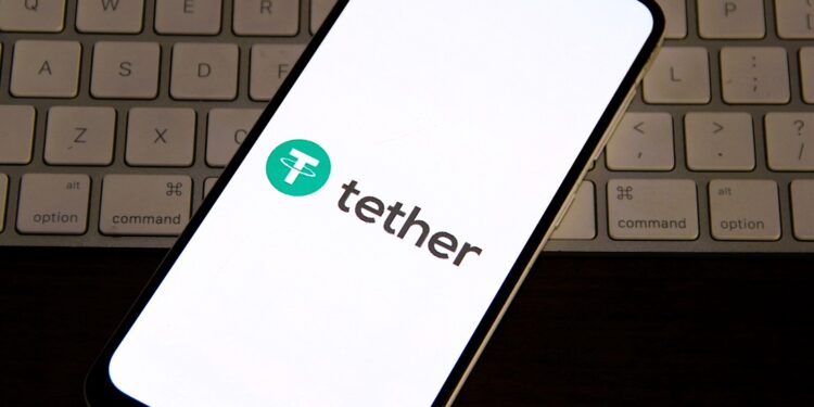 Logo de Tether en un teléfono, arriba de un teclado de computadora.