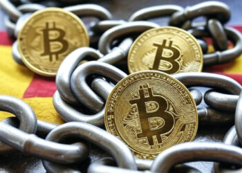 Monedas de Bitcoin encadenadas, sobre la bandera de España.