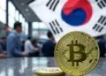 Dos monedas de bitcoin sobre una mesa, al fondo hay una bandera de Corea del Sur