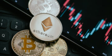 moneda de ethereum sobre monedas de bitcoin junto a pantalla con grafico de precio