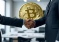 dos ejecutivos dándose la mano y un bitcoin de fondo.