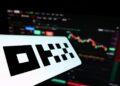 Una pantalla con el logo del exchange OKX delante de un gráfico de precios.