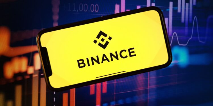 Logo de Binance sobre una pantalla de un móvil con velas rojas y verdes de fondo que reflejan la volatilidad del mercado.