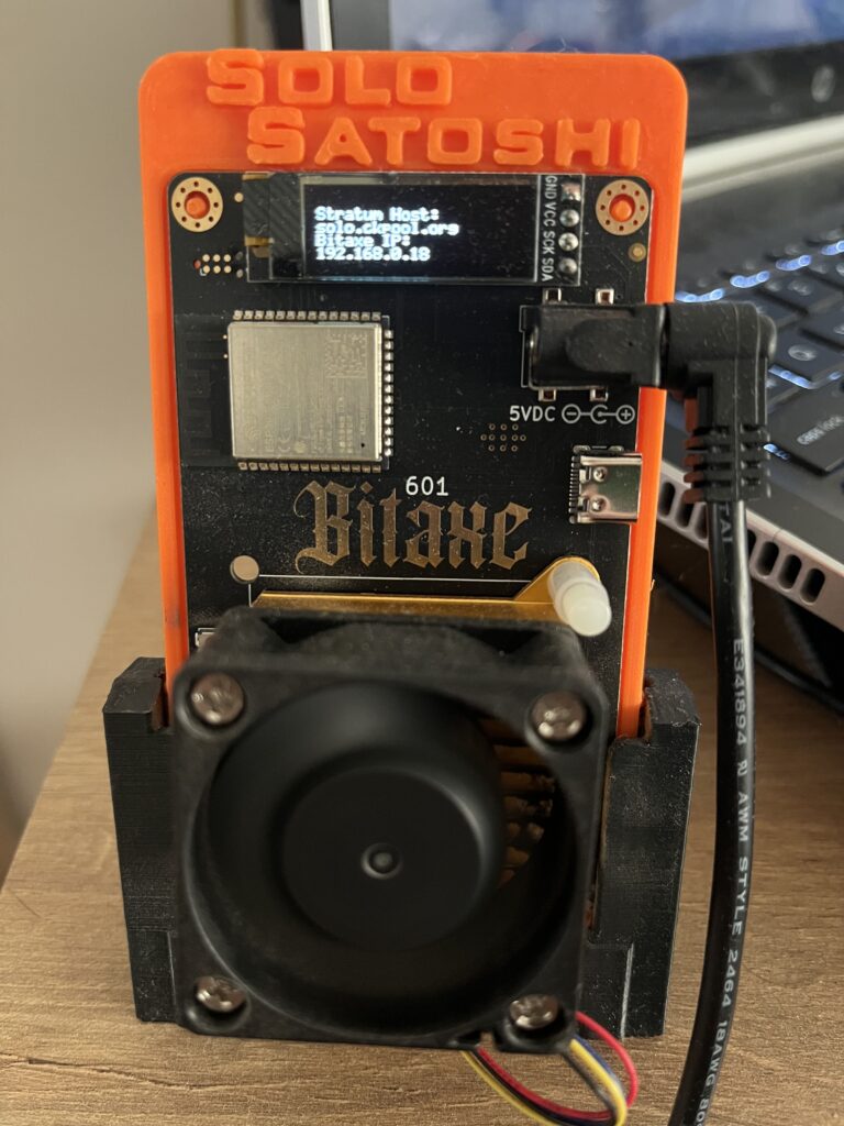 Un mini asic destinado a la minería de Bitcoin en un escritorio de color madera.