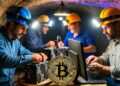 Hombres trabajando en una cueva minera junto a computadoras y una moneda de Bitcoin dorada.
