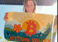 Una mujer sonrie mientras muestra un lienzo con una B en naranja y el nombre de Bitcoin Valley.