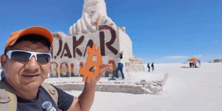 Una persona sostiene en alto un logo color naranja de bitcoin en las salinas de Bolivia.