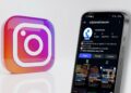 Logo de Instagram con celular a su derecha con la nueva cuenta de CriptoNoticias en su pantalla.