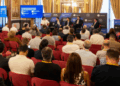 Un grupo de expectadores frente a un panel en un foro de criptomonedas en un auditorio de España.