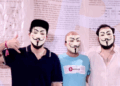 3 jovenes lucen máscara de Anonymous frente a pendón del Libro Blanco de Bitcoin.