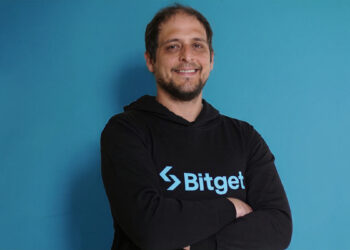 Sibre un fondo azul: Hombre con sudadera negra que tiene el logo de Bitget en color azul. Es Alejandro Blanco, director de Desarrollo de Negocios de Bitget.