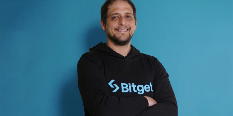 Sibre un fondo azul: Hombre con sudadera negra que tiene el logo de Bitget en color azul. Es Alejandro Blanco, director de Desarrollo de Negocios de Bitget.