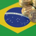 Monedas físicas de bitcoin doradas sobre la parte superior derecha de la bandera de Brasil.