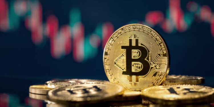 Bitcoin sobre una mesa y gráficas de mercado en el fondo.