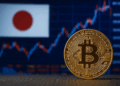 Imagen realista que muestra una moneda dorada de Bitcoin en primer plano, enfocada sobre una superficie oscura. Al fondo se distingue una bolsa de valores japonesa, con gráficos financieros ascendentes y la bandera de Japón desenfocada. Representa la conexión entre Bitcoin y el mercado financiero japonés.