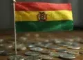 Bandera de Bolivia sobre varias monedas físicas arriba de una mesa.