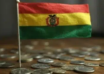 Bandera de Bolivia sobre varias monedas físicas arriba de una mesa.