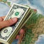 Dólares sostenidos por una mano con un fondo del continente americano.