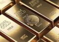Lingotes de oro organizados con una moneda física de bitcoin dorada.