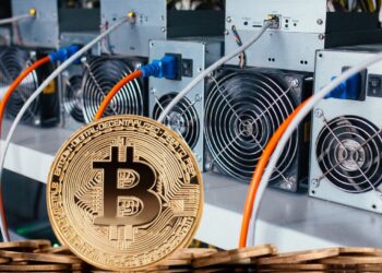 Moneda física de bitcoin dorada con mineros ASIC detrás.