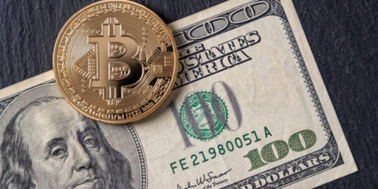 Moneda física de bitcoin dorada sobre un billete de 100 dólares sobre una mesa.