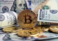 Moneda física de bitcoin dorada rodeada de billetes de 100 dólares estadounidenses.
